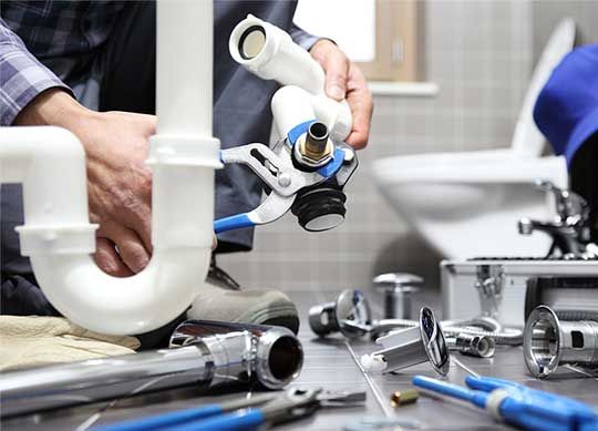 Plumber repairing a pipe under a sink at night